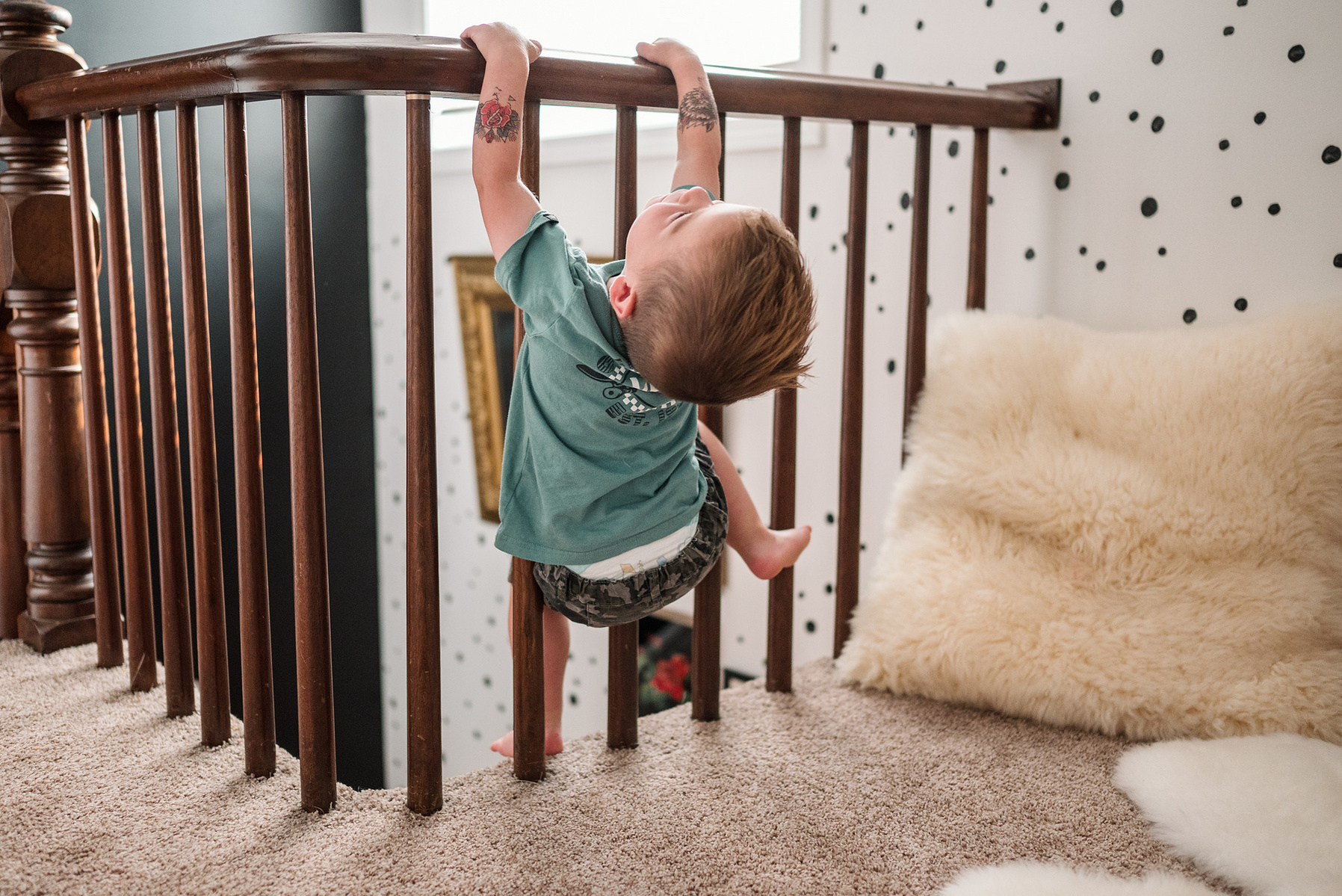 A young boy hangs from the banister and laughs during their boston in home family photography session