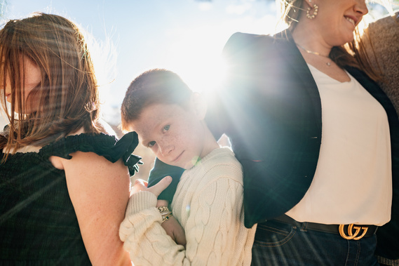 A red haired boy looks directly at the camera while the sun shines behind his head during a Cambridge family photo shoot
