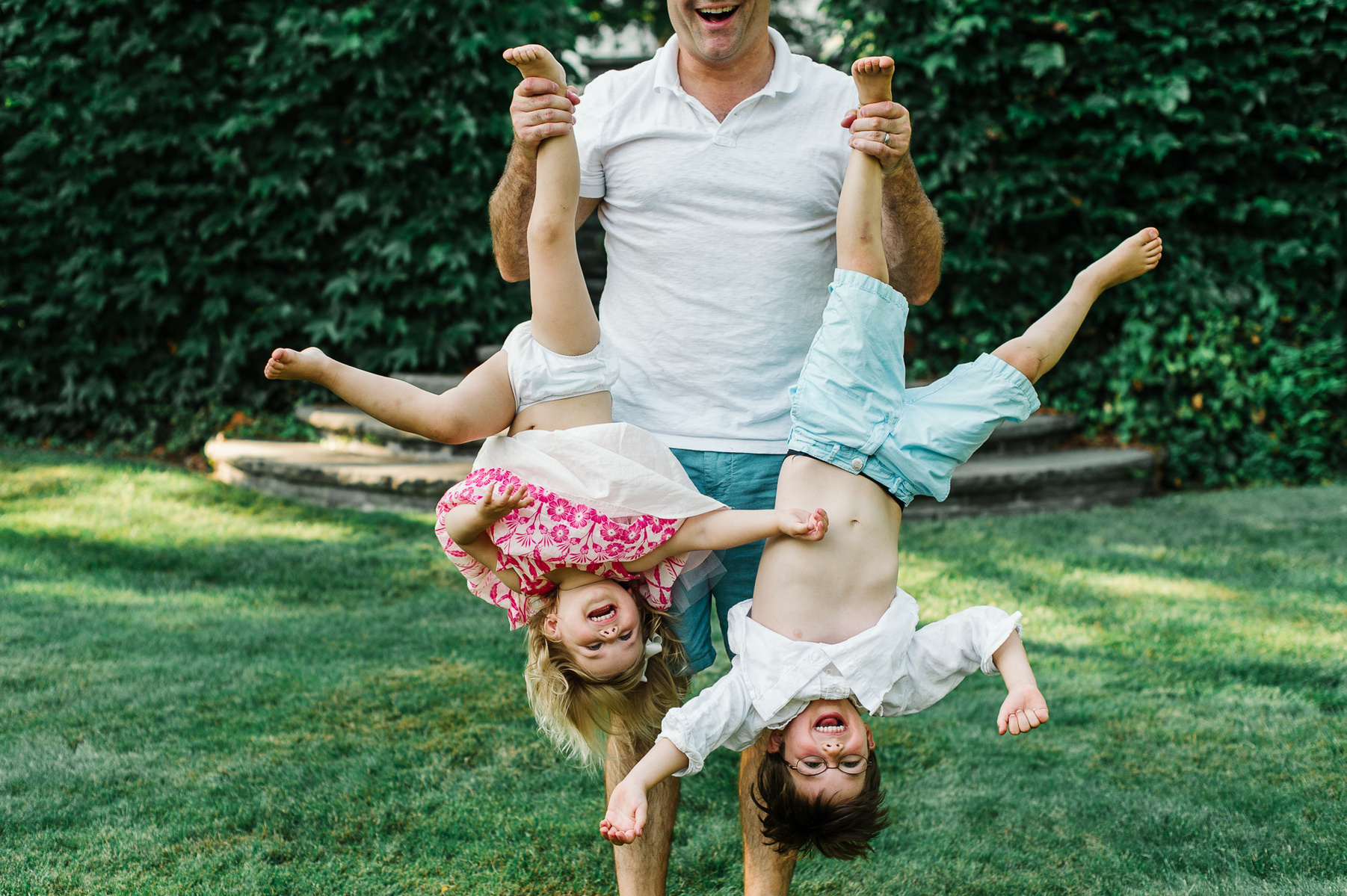 A father playfully holds his two children upside down by their ankles at their fun boston family photography session
