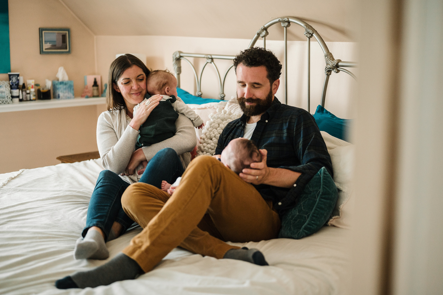 Parents snuggle their newborn twins while sitting on their bed