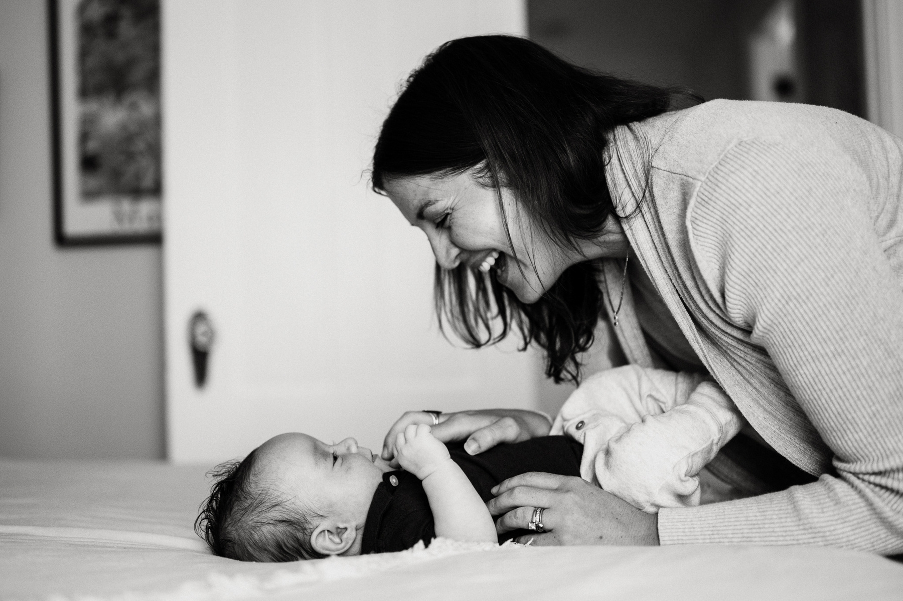 A mother smiles and leans over her newborn twin laying on a bed.
