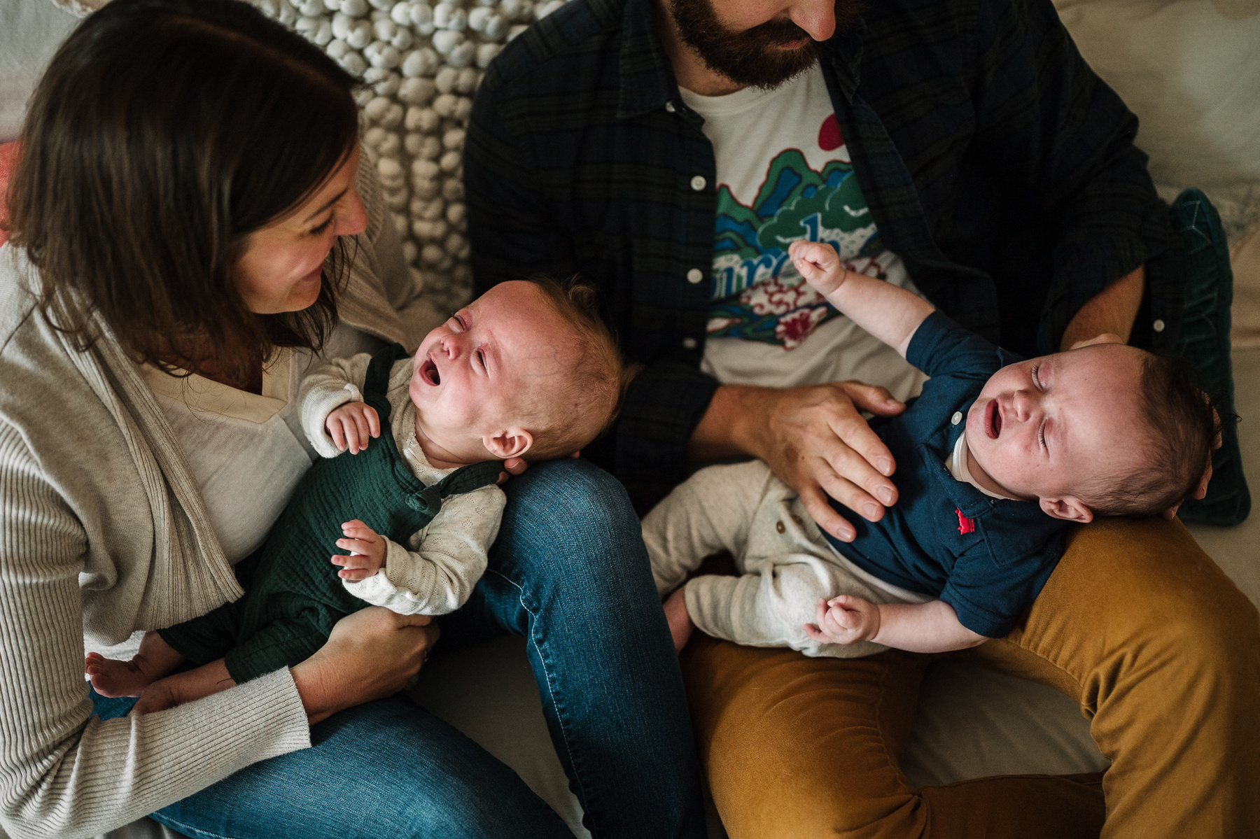 Newborn twins cry while laying on their parents' lap