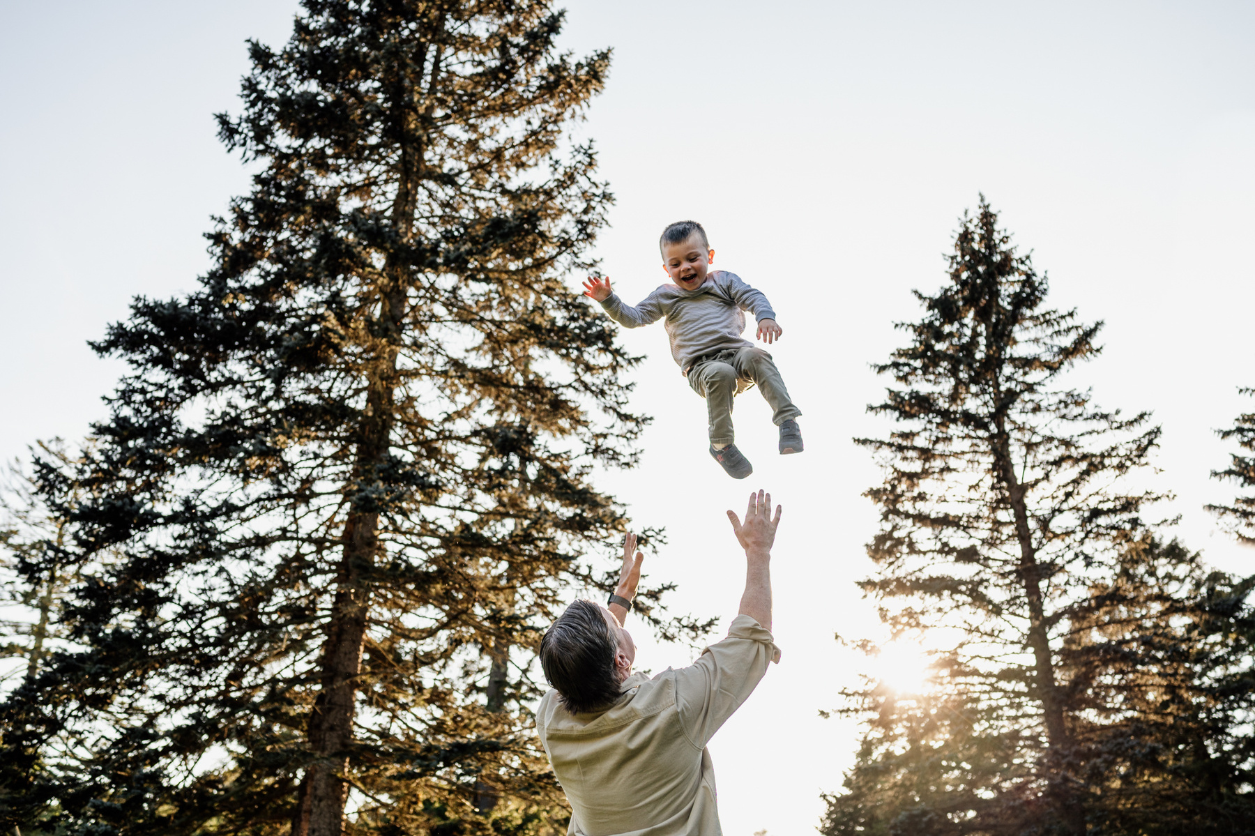 A father throws his son in the air during their Arnold Arboretum fall mini-session