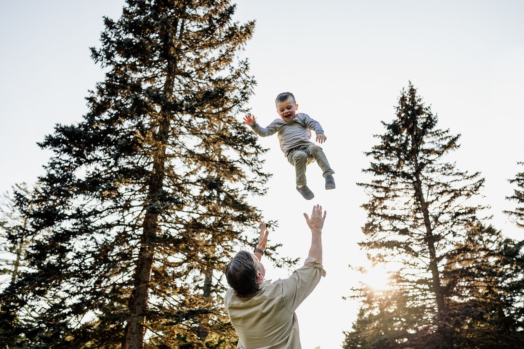 A father throws his son in the air during their Arnold Arboretum fall mini-session