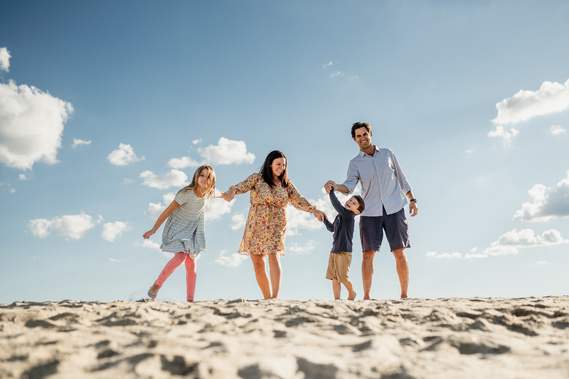 A family of four twirls and smiles on Crane Beach against the sun and blue sky