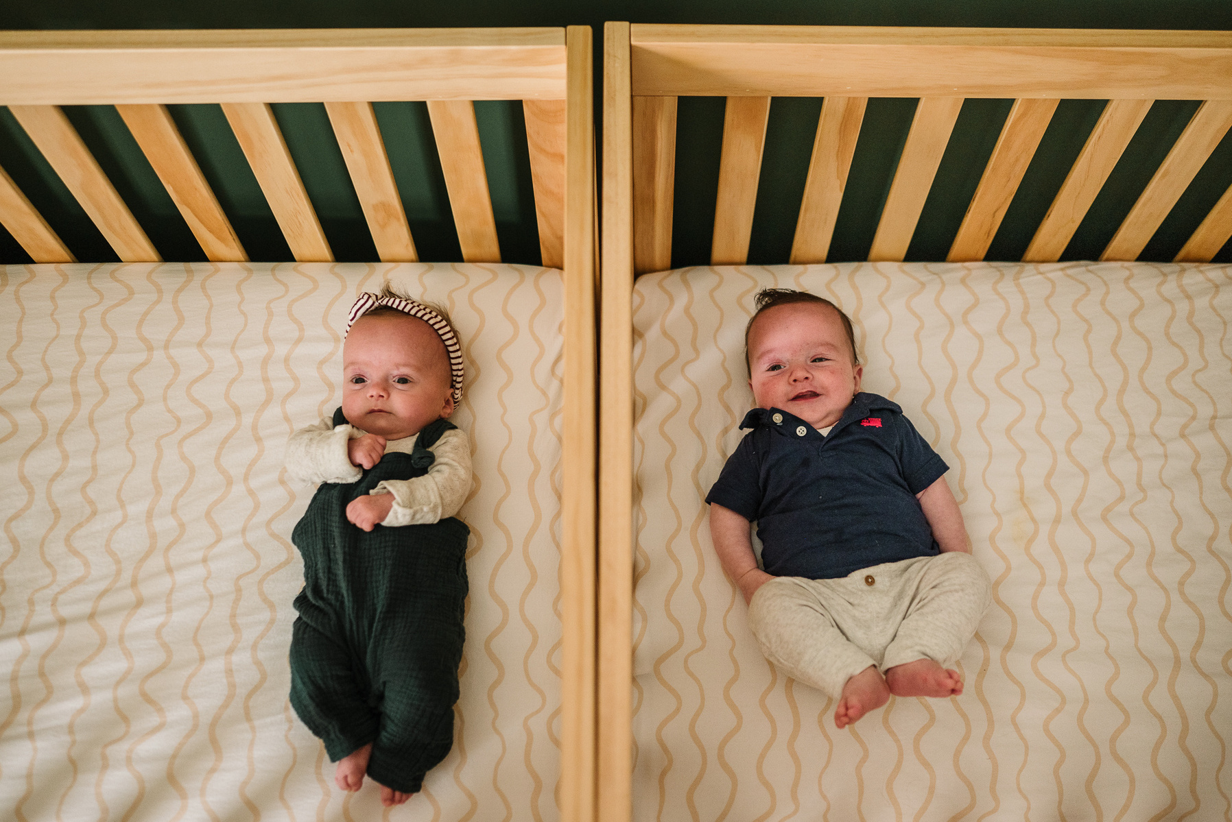 Boston newborn twins lay besides each other in matching cribs
