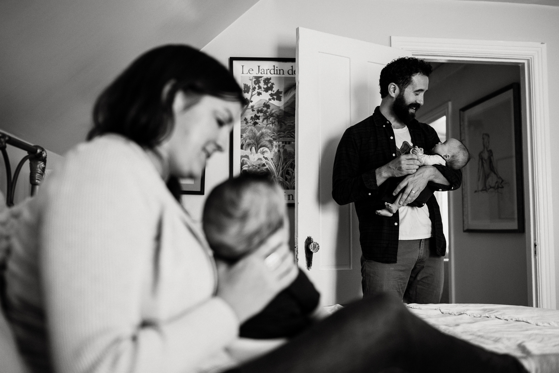 A father holds his newborn twin daughter while a mother in the foreground holds her newborn twin son