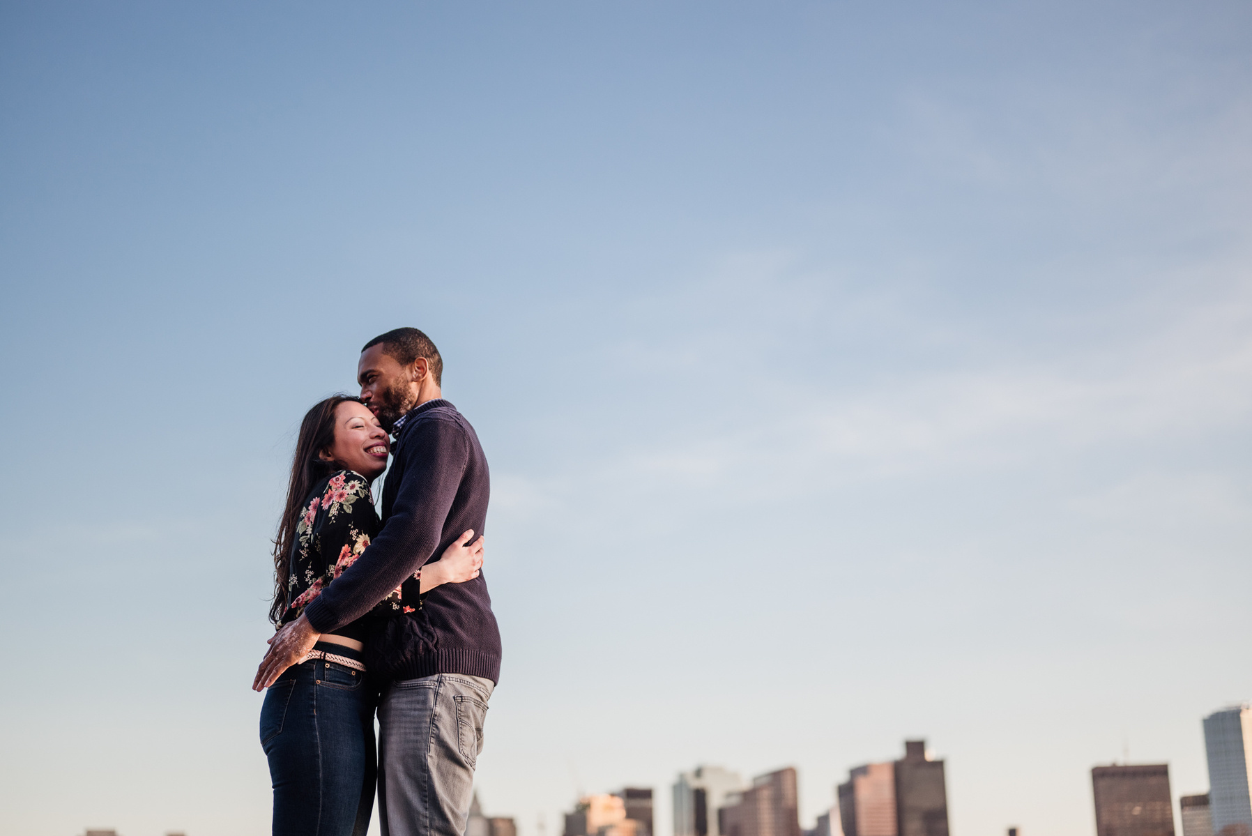 A couples embraces at sunset in front of the boston skyline