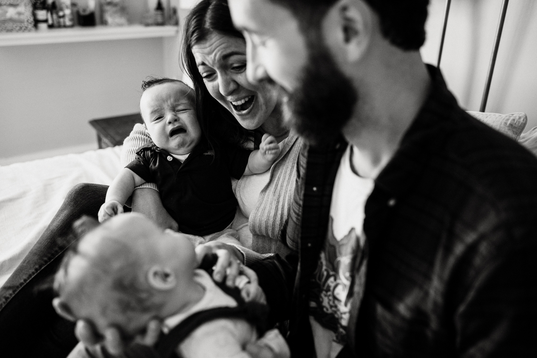 Parents laugh and smile while their newborn twins cry on their laps