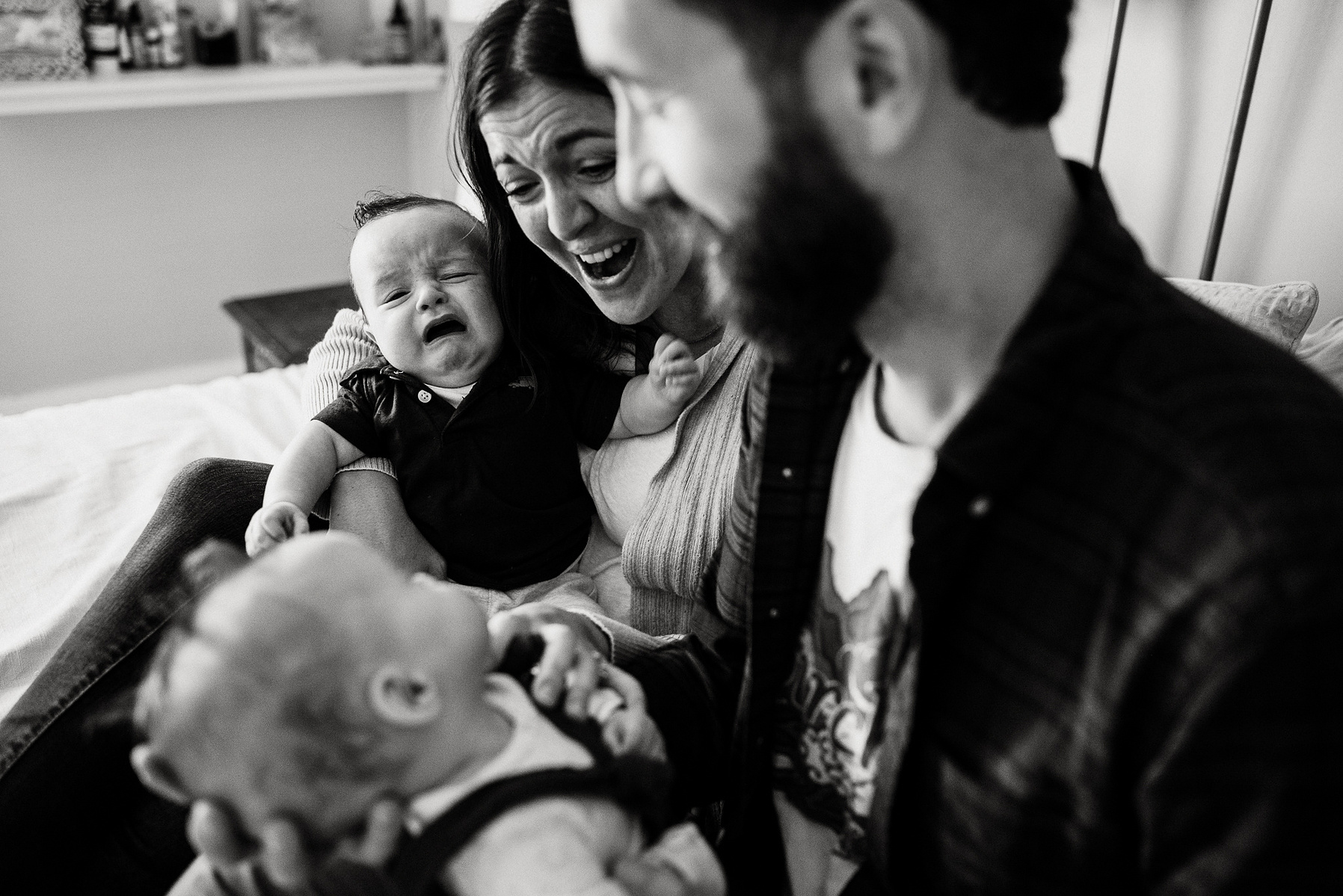 Parents laugh and smile while their newborn twins cry on their laps