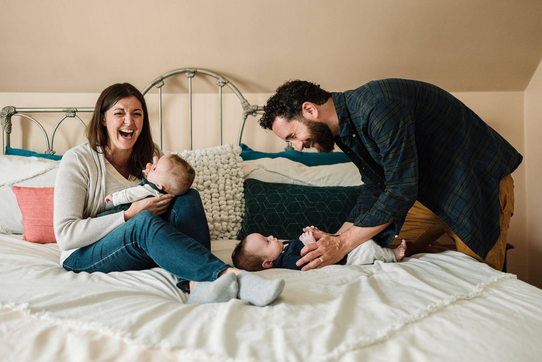 Parents laugh and smile while holding their newborn twins on a bed