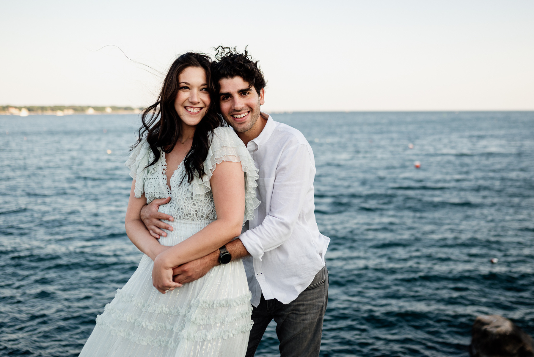 a couple embraces and smiles while standing in front of the ocean during their stage fort park engagement session