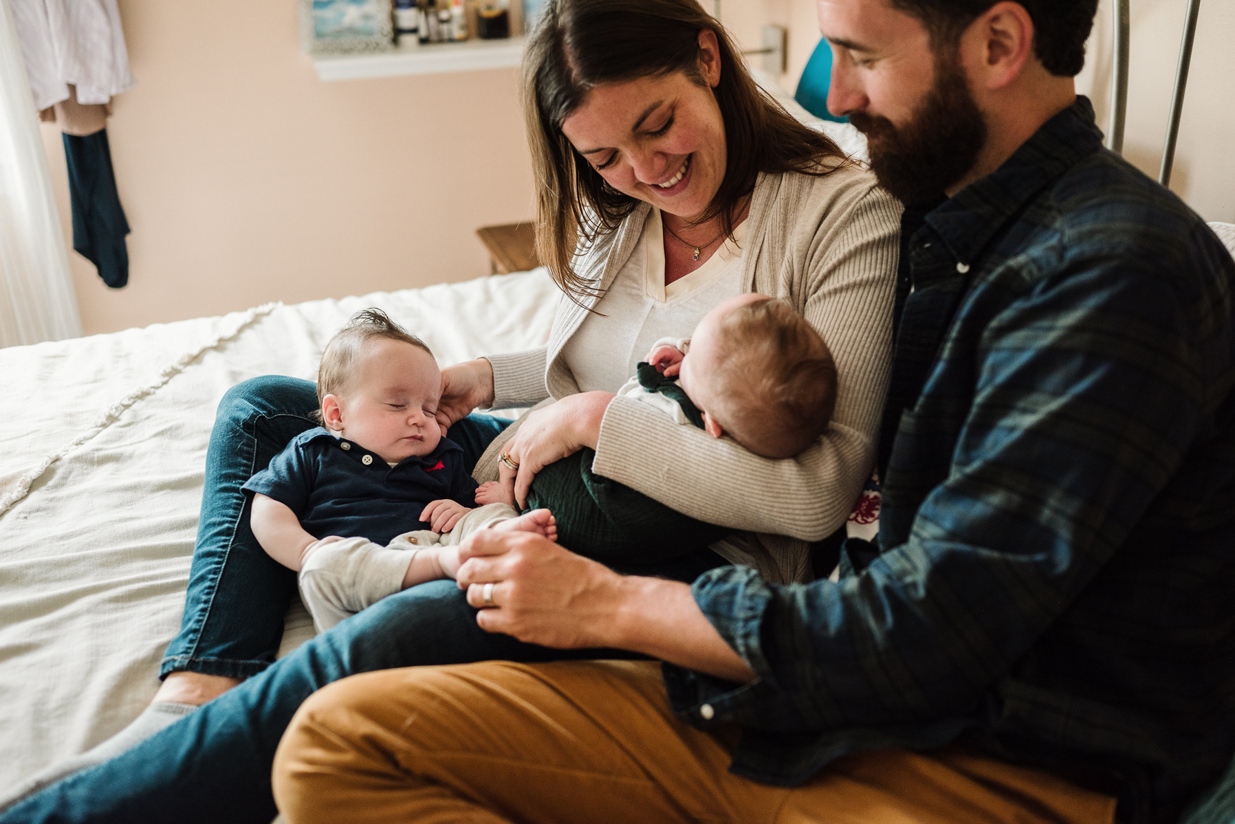 Parents smile and snuggle with their newborn twins on their bed