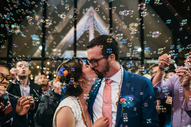 A couple kisses while guests surrounding them blow bubbles into their air during their Camden Snow bowl wedding