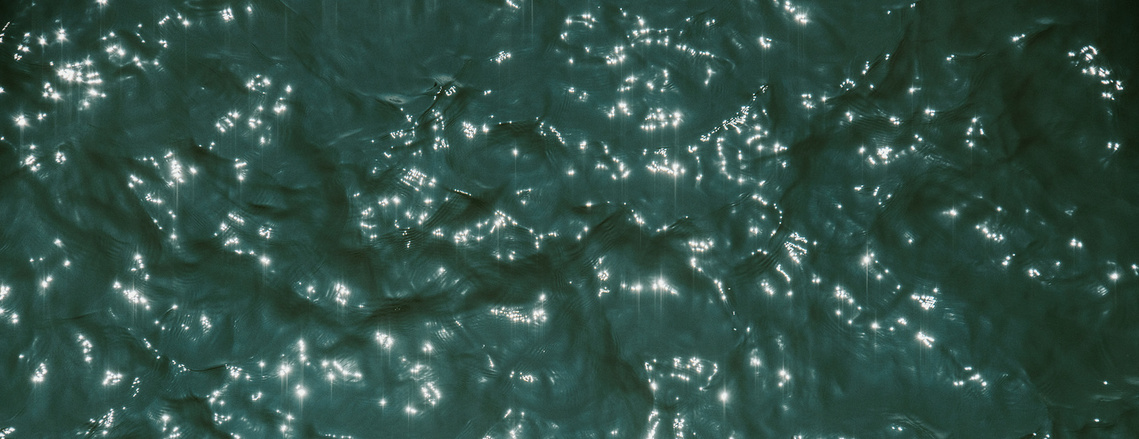 The surface of a dark teal green ocean sparkles in the sunlight