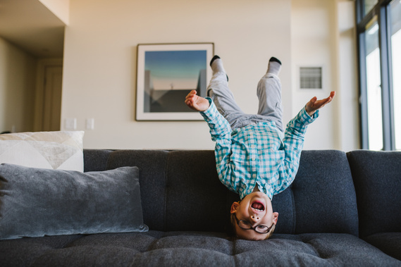 A young boy balances upside down on a grey sofa during a boston family photoshoot