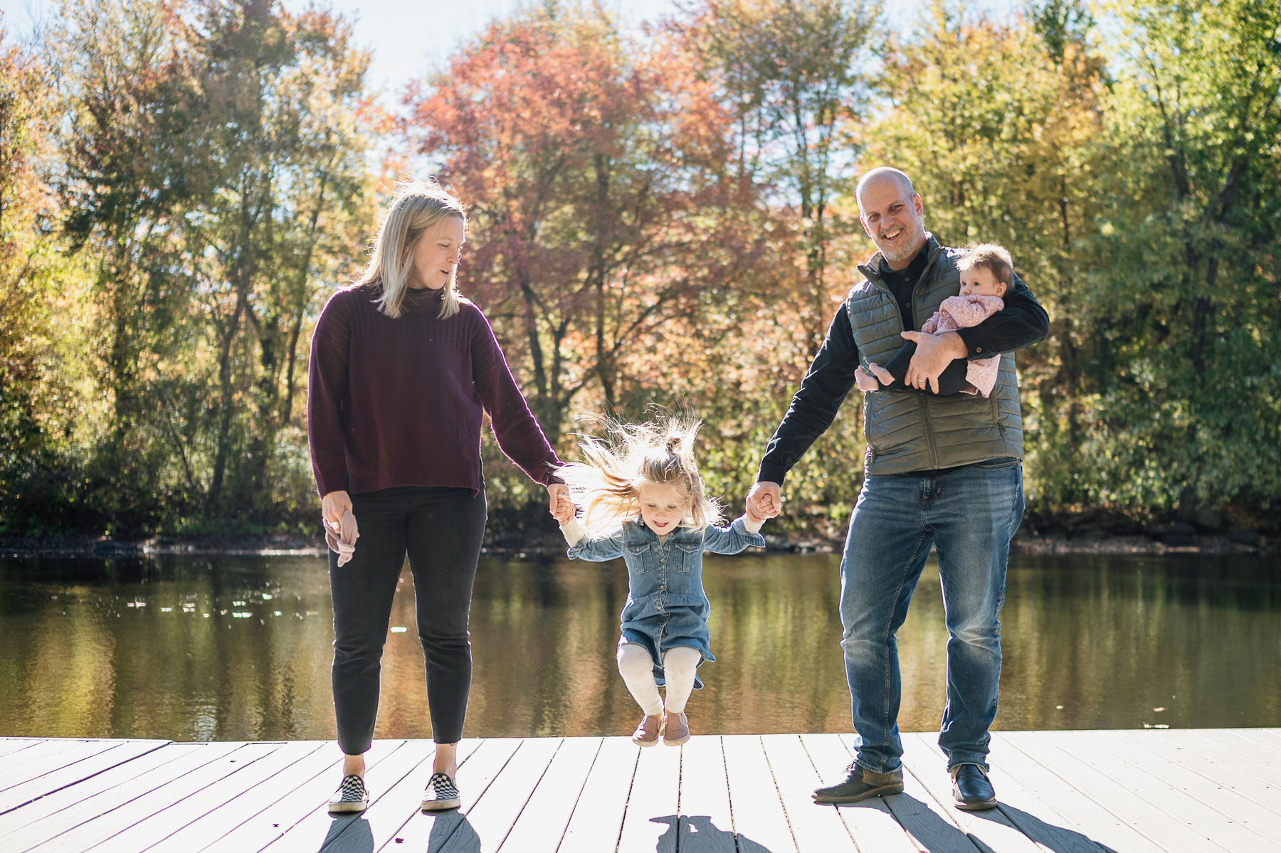 A little girl jumps in front of foliage while her family looks on in Newton during their fall mini-session