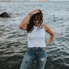 Boston family photographer Korri Leigh Crowley stands in the ocean and smiles while wearing jeans and white tank top