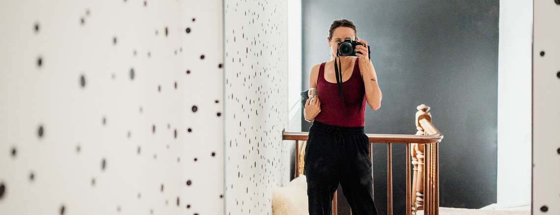 Boston family photographer Korri Leigh Crowley takes a photo of herself in a mirror while standing in a room with black and white polka dot walls