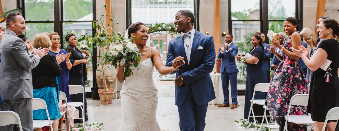 A couple smiles at each other while dancing down the aisle at their Tower Hill Botanic Garden wedding