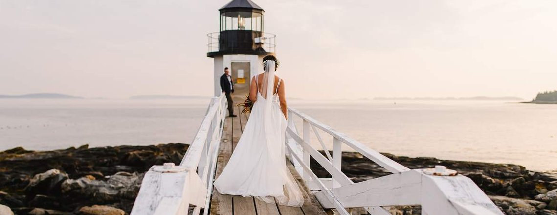 A bride walks towards her groom at the Marshall Point Lighthouse during their Maine adventure elopement. Captured by Boston elopement photographer Korri Leigh Crowley