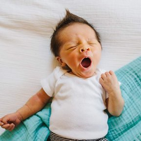 A newborn yawns while laying on a blue and white blanket