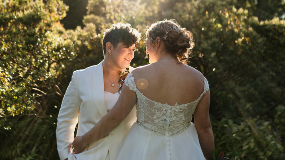 LGBTQ brides pose together while standing in front of greenery and golden sunlight at their Long Hill wedding