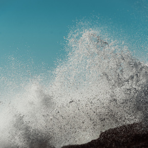 An ocean wave crashes into the air in front of a bright blue sky