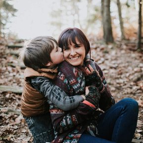 Boston family photographer Korri Leigh crowley is kissed by her young son while sitting in autumn leaves