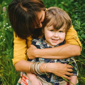Boston elopement photographer Korri Leigh crowley hugs her young son from behind while sitting in tall green grass
