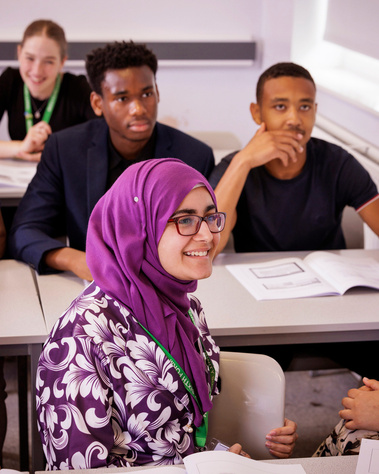 Four college students-two female and two male-engaged in a classroom setting. The female student in the foreground wears a hijab, highlighting diversity and inclusive education at St Margaret Ward Catholic Academy.