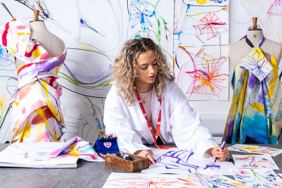 Female fashion design undergraduate student sketching garment concepts in a studio setting, developing creative ideas for her university coursework at Staffordshire University.