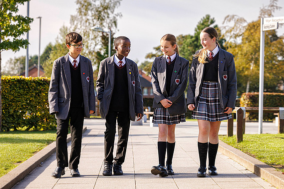 Four secondary school students-two female and two male-walking together through school grounds, smiling and chatting, representing a positive and inclusive learning environment at Oakwood Academy, Nottingham.