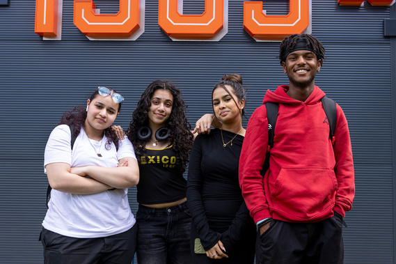 Four college students-three female and one male-standing together, smiling at the camera, representing a diverse and friendly learning environment at Loughborough College.