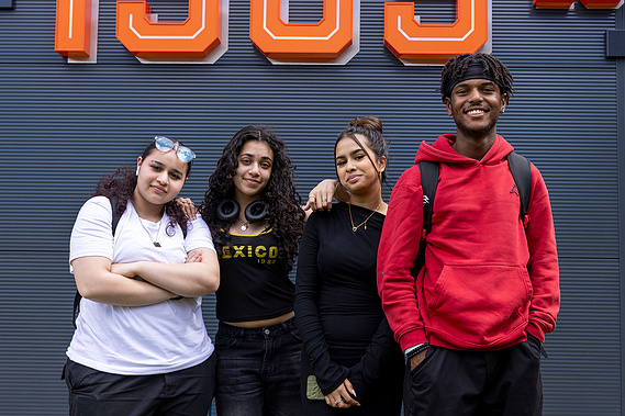 Four college students-three female and one male-standing together, smiling at the camera, representing a diverse and friendly learning environment at Loughborough College.