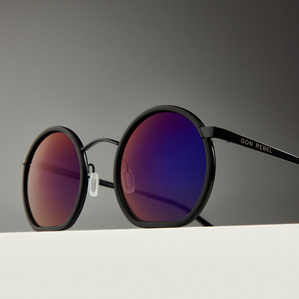 Round black rimmed mirrored multicolor purple blue lens sunglasses sitting on a white surface with a gray background in soft light