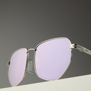 Angular stainless steel rimmed mirrored pink lens sunglasses sitting on a white surface with a gray background in soft light