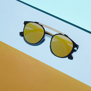 yellow mirrored lens sunglasses with blue and gold metal frame placed by orange and blue paper surfaces