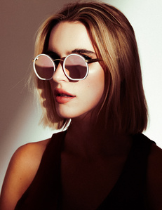 Chloe Holmes woman model headshot profile with blonde hair circular mirrored colorful sunglasses with half of face illuminated by light and other half covered in dark moody shadows in front of white background photographed by William Gormley