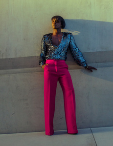 moody colorful portrait Young black african amercian male model with bob haircut wearing pink pants and sequin shirt standing in front of gray concrete wall