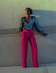 Young black african amercian male model with bob haircut wearing pink pants and sequin shirt standing in front of gray concrete wall