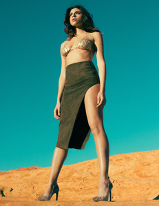 brunette female woman model wearing high heals green skirt and metal gold chain bra standing on orange and yellow rock formation with blue skies in background photographed by william gormley
