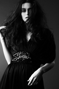 moody portrait monochrome medium closeup of Ruby King female model standing wearing black jumpsuit with sequin belt with right arm touching her dark brown hair in dark shadowy light photograph by william gormley