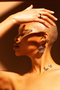 shadowy background illuminated face close up face profile topless bald light skin young woman model Fitz right hand raised over head creating shadow on face wearing jewelry rings earings designed by german kabirski, photograph by william gormley