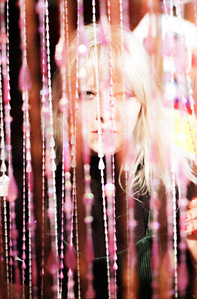 colorful portrait blonde female model wearing black looking through pink beaded curtain