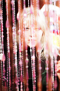 blonde female model wearing black looking through pink beaded curtain
