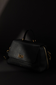 Black leather gold plated buckle and gold zipper designer handbag by ectu placed in the shadows with dark background with a small corner of the bag partially lit.