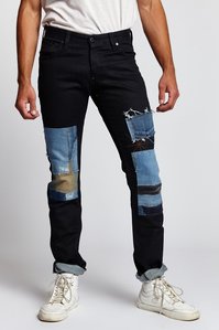 lower half of male model legs wearing black denim jeans with blue denim patches and white sneakers on white background