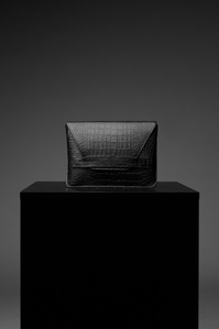 Black leather clutch purse sitting on a black cube box with a dark grey background basking in soft light