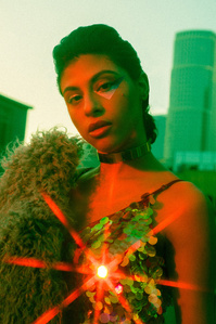 brunette female model close up of her face with hair in bun wearing sequin top with star filter flare and fur coat over her shoulder with red light illuminating her face  with sky line and buildings in background 